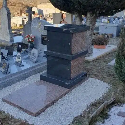 Monument funéraire en granit conçu pour accueillir des urnes funéraires, installé dans un cimetière avec un aménagement soigné en gravier.