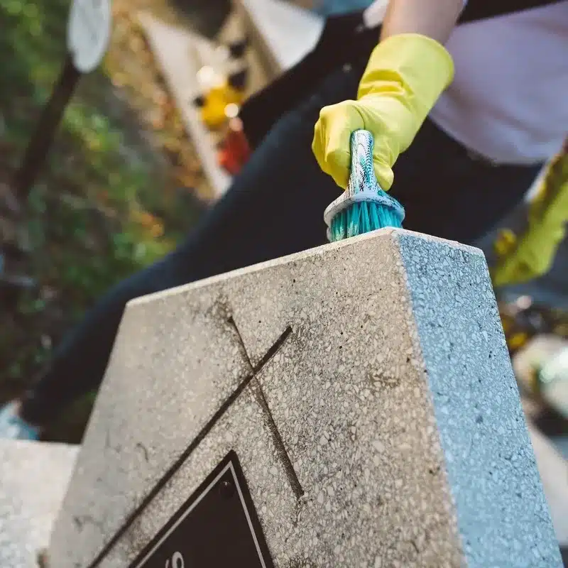 Nettoyage et entretien d’une stèle funéraire avec une brosse, mettant en valeur la restauration des inscriptions sur le monument.