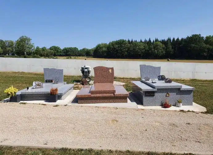monument-funeraire-tombes Trois monuments funéraires en granit installés sur une parcelle aménagée, avec des plaques commémoratives et ornements, sous un ciel dégagé et un cadre verdoyant. 