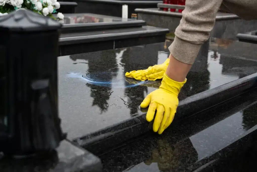 Main essuyant un monument funéraire près d’une lanterne rouge, illustrant l’entretien d’une sépulture pour préserver son éclat.