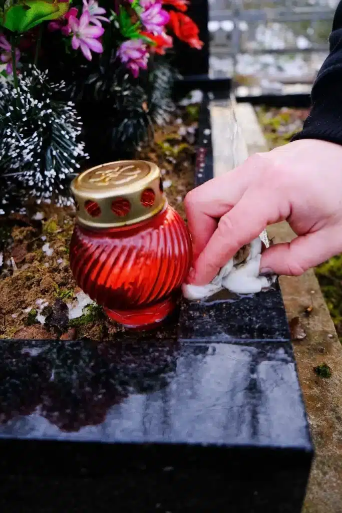Main essuyant un monument funéraire près d’une lanterne rouge, illustrant l’entretien d’une sépulture pour préserver son éclat.
